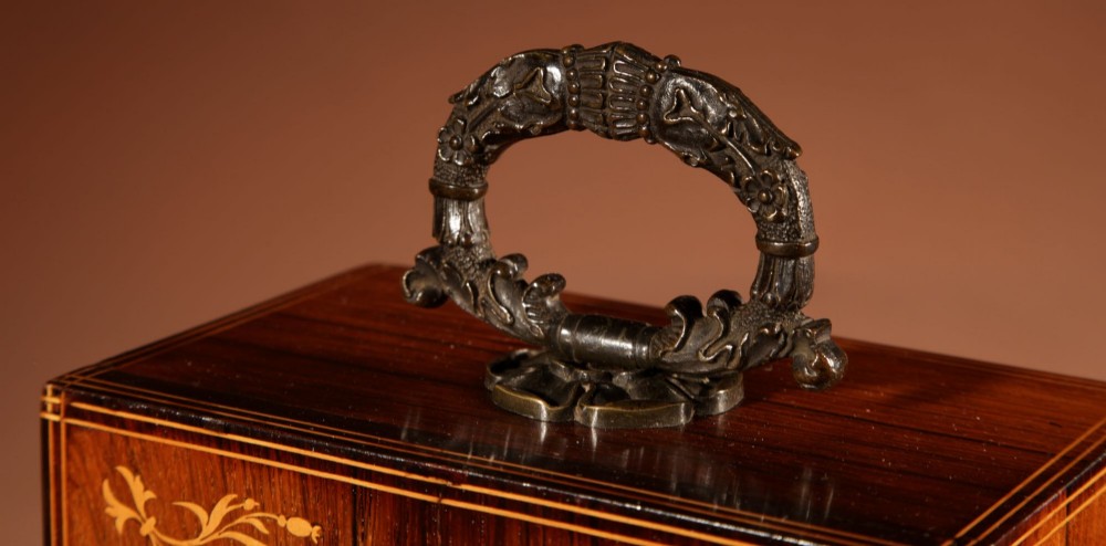 A rectangular Charles X dark rosewood mantel clock featuring intricate floral marquetry inlay, a circular silvered dial with Roman numerals, and a cast brass carrying handle on top. View V