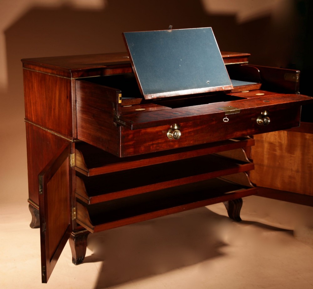A Regency mahogany library secretaire featuring a pull-out writing drawer with an adjustable slope, brass handles, and lower cabinet doors opening to reveal pull-out tray shelves.
