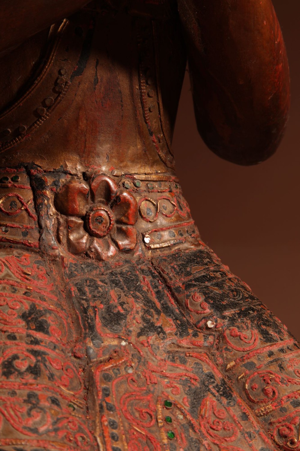 A carved wooden Thai Thepphanom guardian statue depicted kneeling with hands held in a prayer gesture, featuring a conical headdress and gilded red lacquered details. View VI