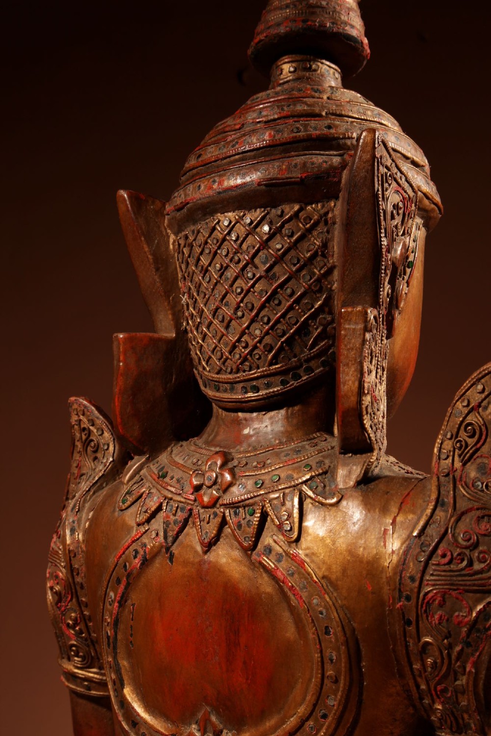 A carved wooden Thai Thepphanom guardian statue depicted kneeling with hands held in a prayer gesture, featuring a conical headdress and gilded red lacquered details. View XIII