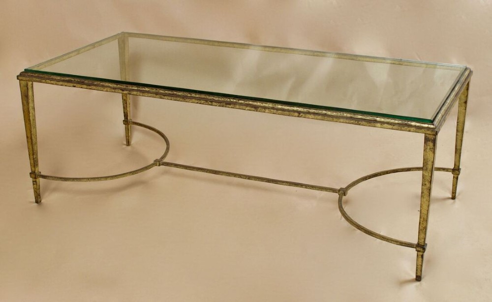 A rectangular gilded wrought iron coffee table featuring a clear glass inserted top and a curved stretcher base.