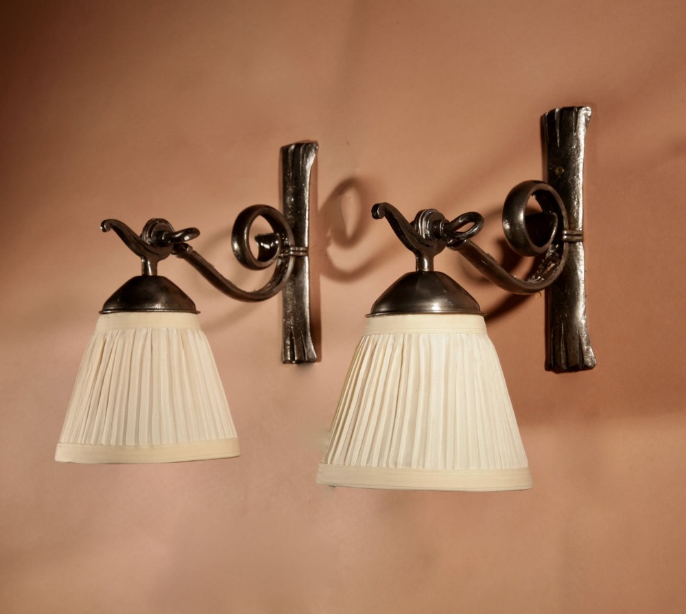 A pair of Art Deco wrought iron wall sconces featuring curved scroll arms and conical pleated cream fabric shades mounted on wall brackets. View II