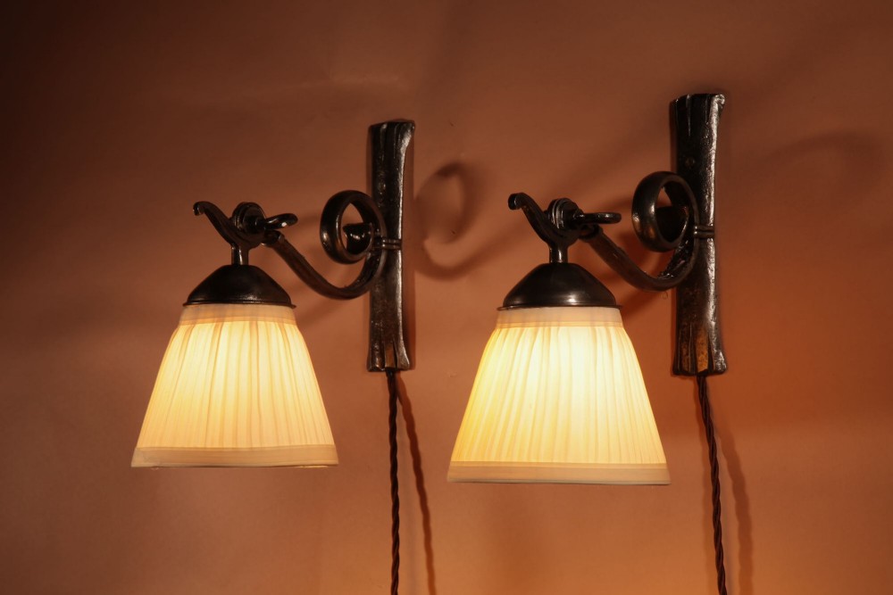 A pair of Art Deco wrought iron wall sconces featuring curved scroll arms and conical pleated cream fabric shades mounted on wall brackets. View III