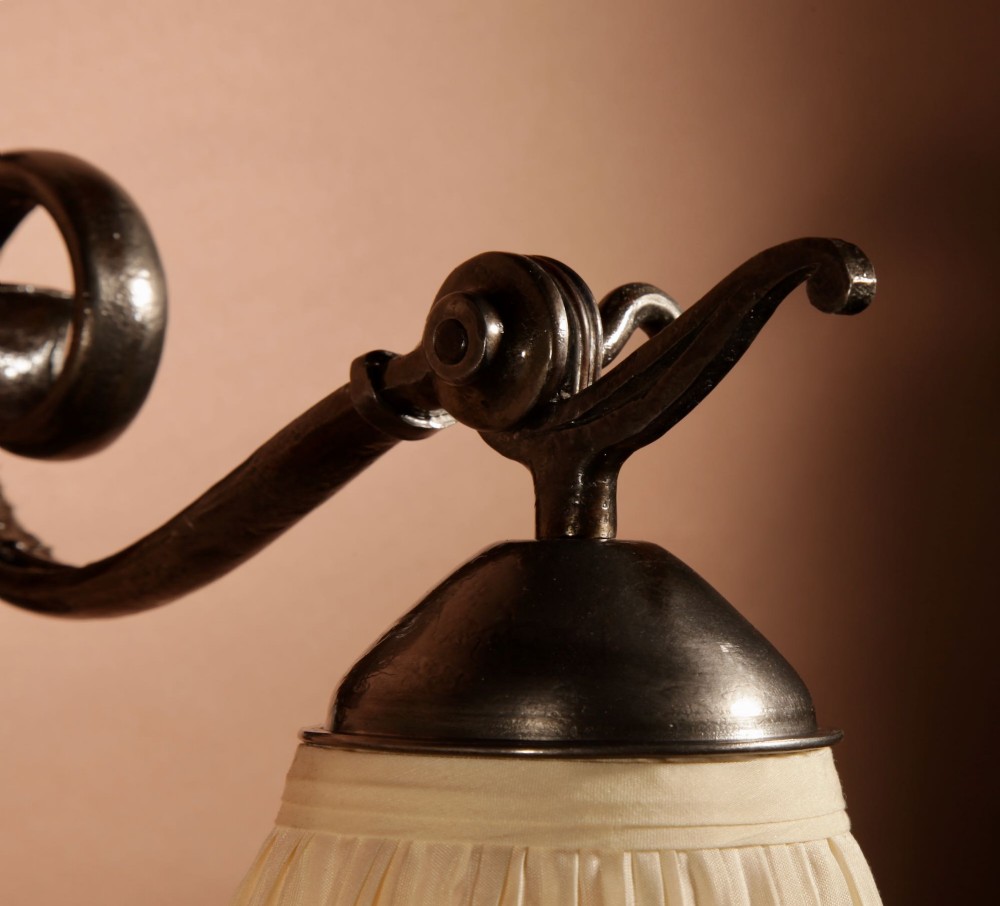 A pair of Art Deco wrought iron wall sconces featuring curved scroll arms and conical pleated cream fabric shades mounted on wall brackets. View V