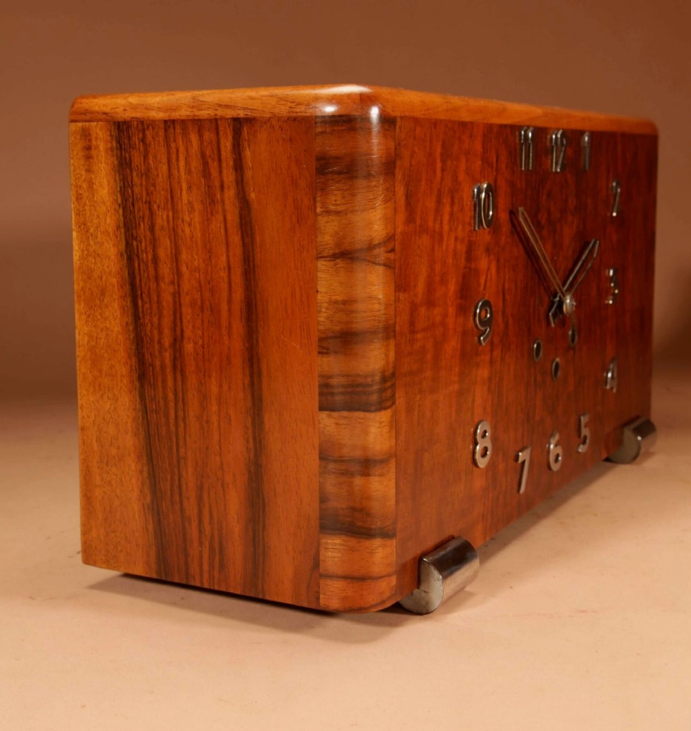 A horizontal rectangular Art Deco walnut mantel clock with applied chrome Arabic numerals, chrome hands, and polished metal bracket feet. View III