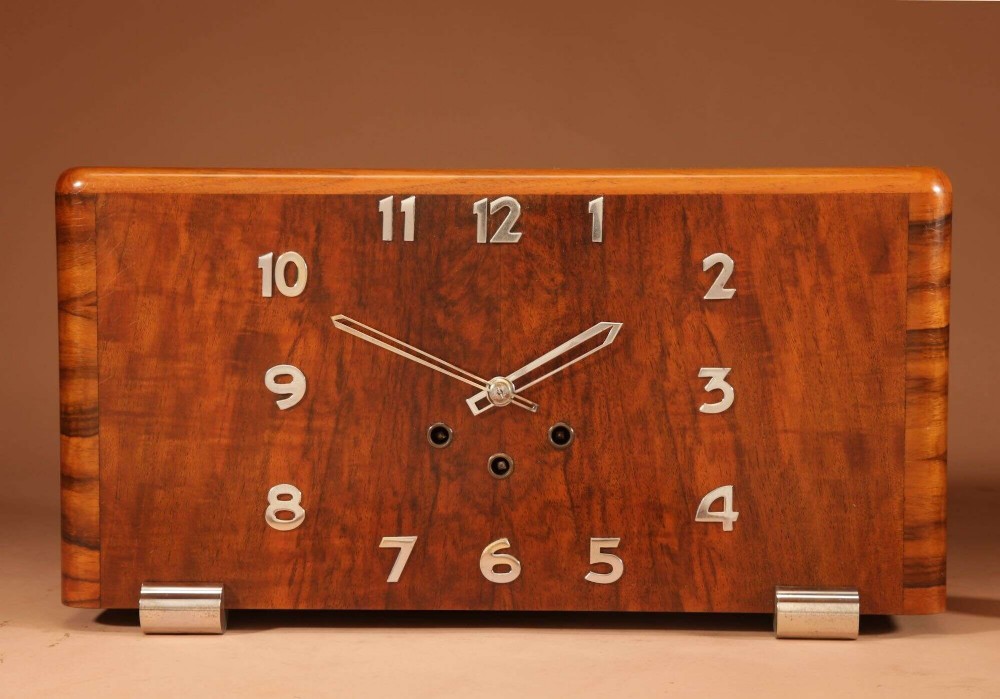 A horizontal rectangular Art Deco walnut mantel clock with applied chrome Arabic numerals, chrome hands, and polished metal bracket feet. View VI
