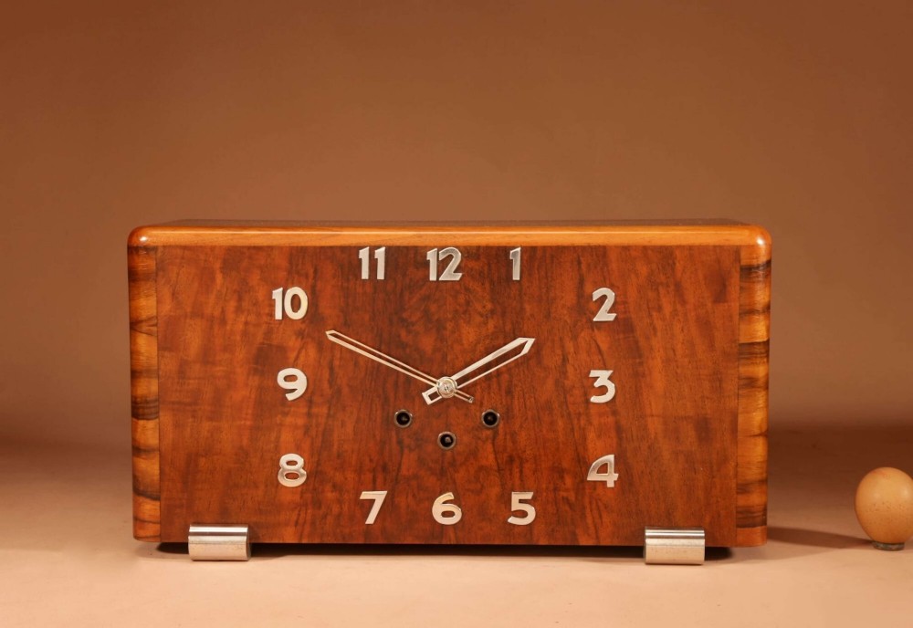 A horizontal rectangular Art Deco walnut mantel clock with applied chrome Arabic numerals, chrome hands, and polished metal bracket feet.