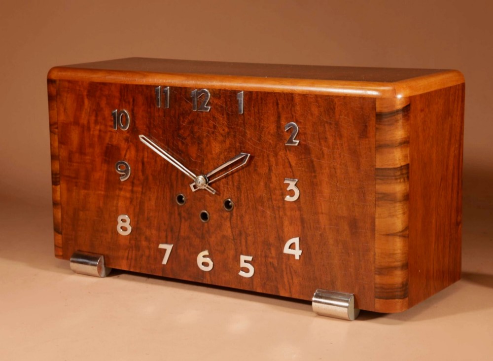 A horizontal rectangular Art Deco walnut mantel clock with applied chrome Arabic numerals, chrome hands, and polished metal bracket feet. View VII