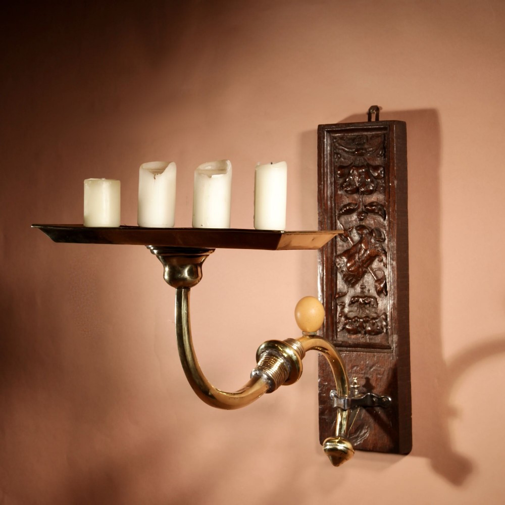 A wall-mounted candle sconce featuring a carved dark oak backboard and a curved brass arm holding a tray with four white candles. View II