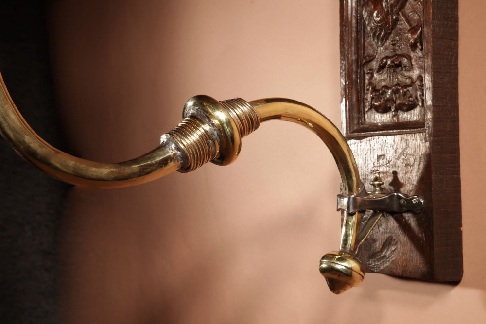 A wall-mounted candle sconce featuring a carved dark oak backboard and a curved brass arm holding a tray with four white candles. View VIII