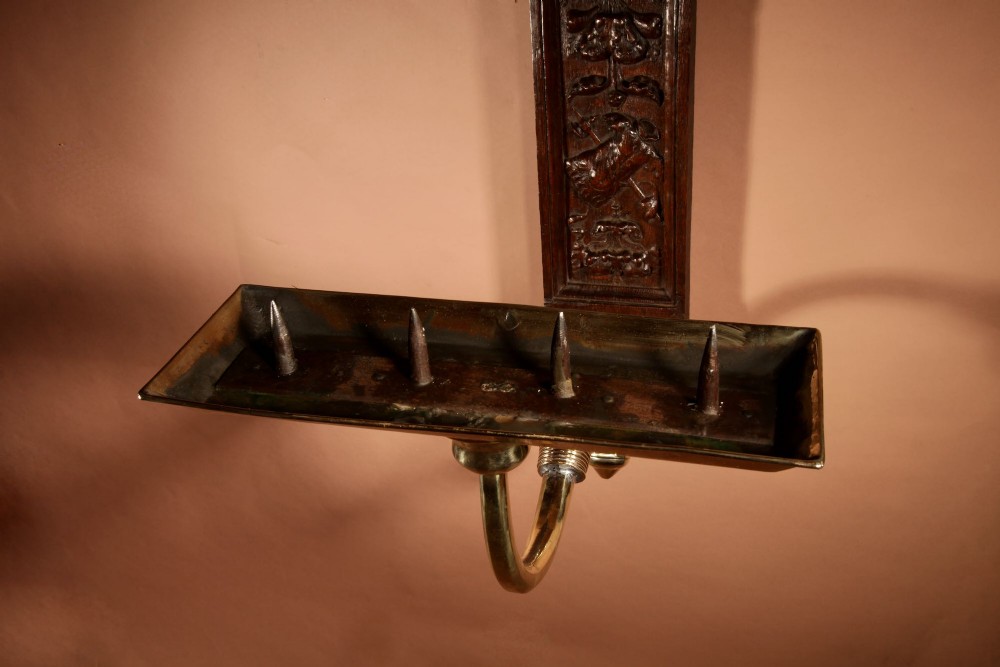 A wall-mounted candle sconce featuring a carved dark oak backboard and a curved brass arm holding a tray with four white candles. View XI