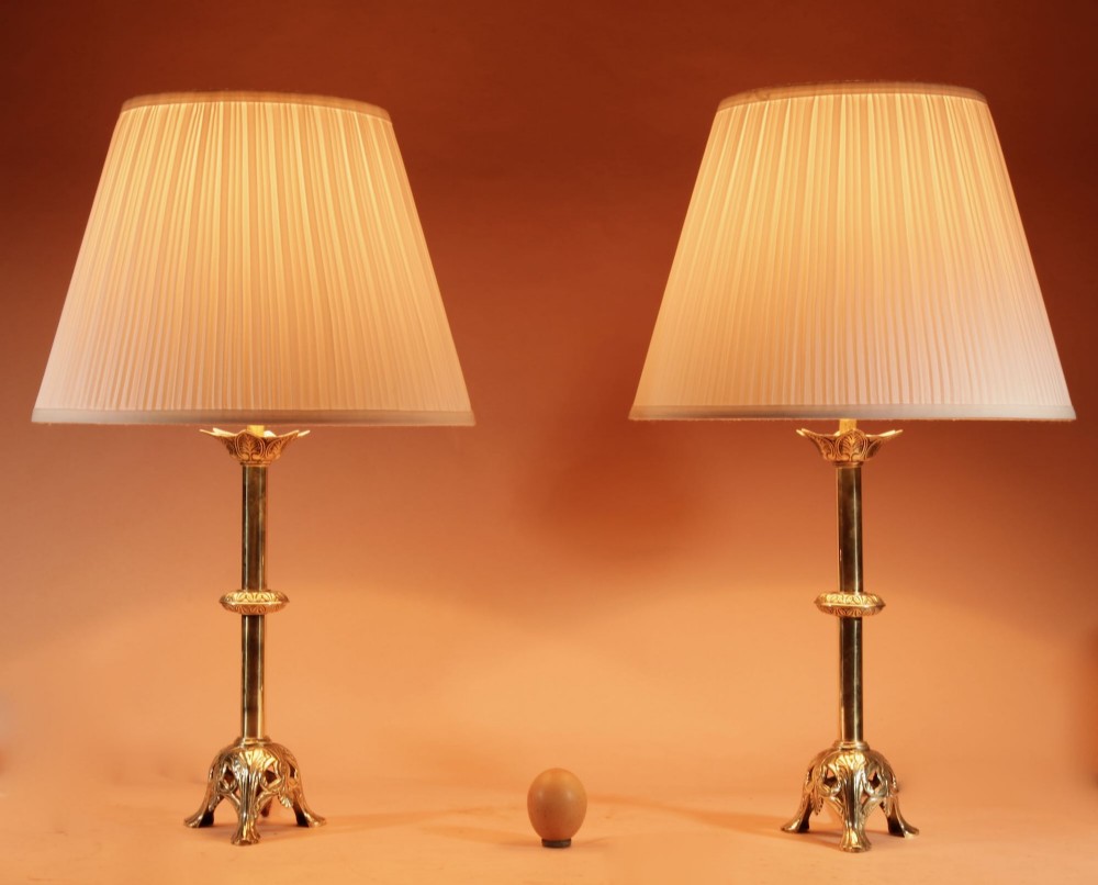 A pair of cast brass table lamps featuring knopped columns, pierced foliage bases, and off-white pleated shades.