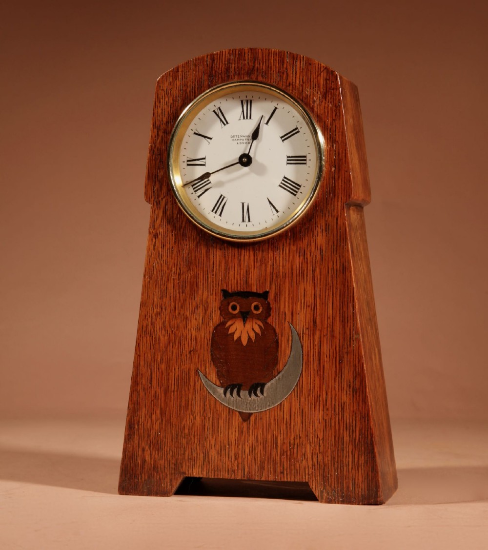 An Arts and Crafts tapered oak mantel clock featuring a white circular dial and wood inlay depicting an owl perched on a pewter crescent moon. View II