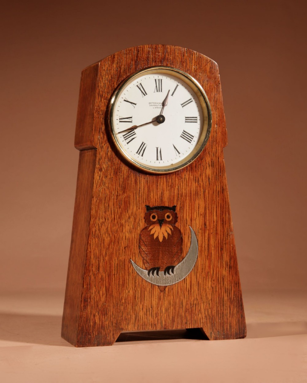 An Arts and Crafts tapered oak mantel clock featuring a white circular dial and wood inlay depicting an owl perched on a pewter crescent moon. View III