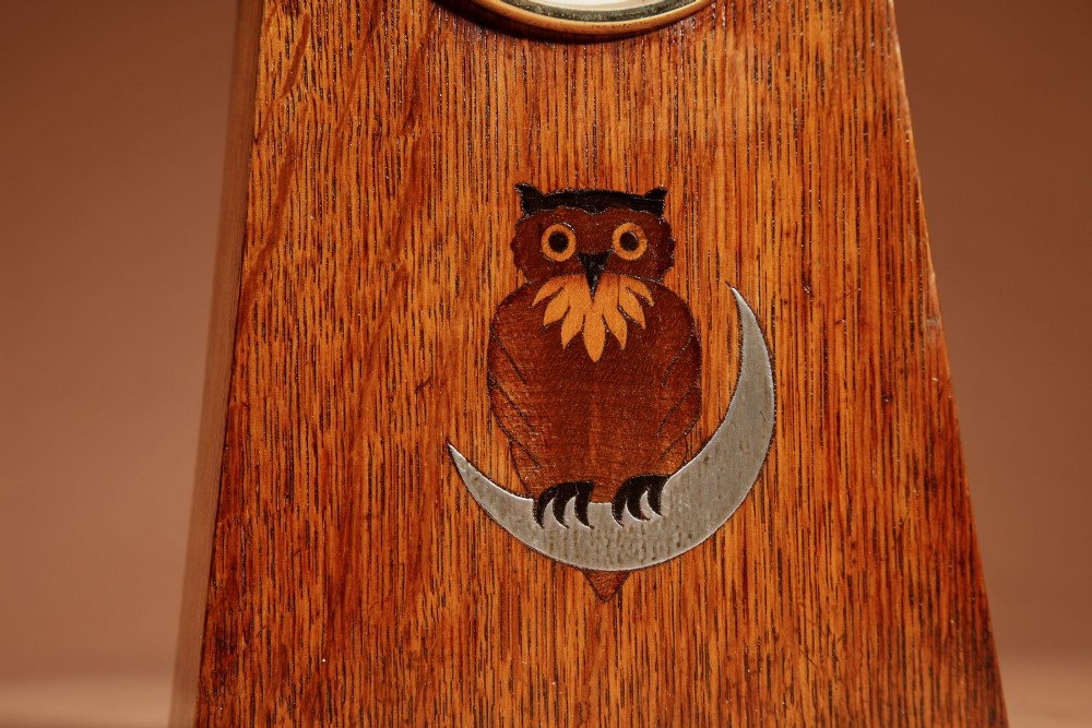 An Arts and Crafts tapered oak mantel clock featuring a white circular dial and wood inlay depicting an owl perched on a pewter crescent moon. View IV