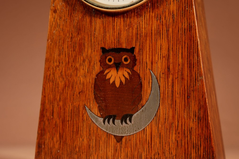 An Arts and Crafts tapered oak mantel clock featuring a white circular dial and wood inlay depicting an owl perched on a pewter crescent moon. View V