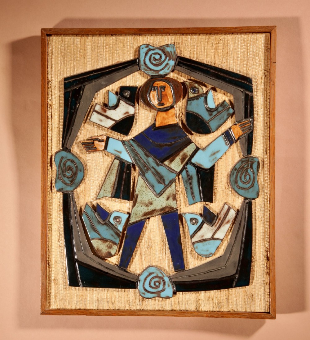A framed mid-century modern ceramic wall relief featuring stylised figures and birds in turquoise and blue glazes mounted on a woven background.