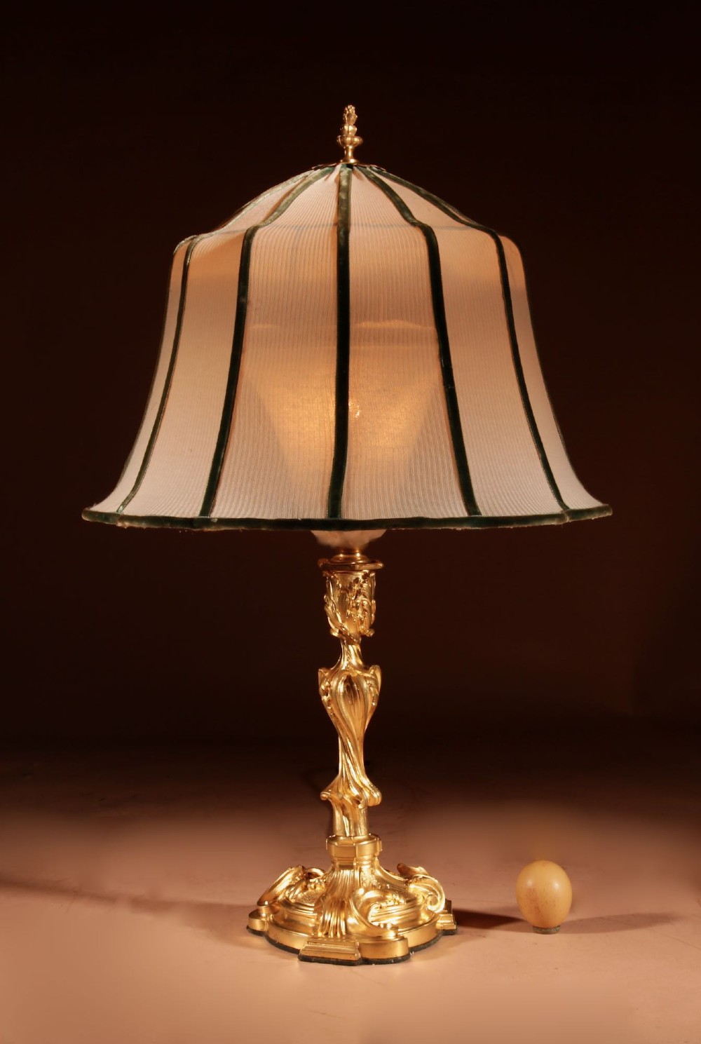 A French Rococo style gilded bronze table lamp featuring an asymmetrical scrolling base and a fitted fabric shade with dark green vertical trim.