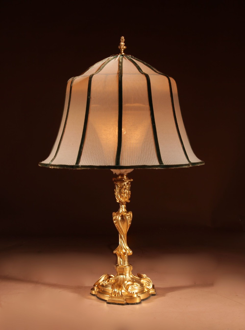 A French Rococo style gilded bronze table lamp featuring an asymmetrical scrolling base and a fitted fabric shade with dark green vertical trim. View II