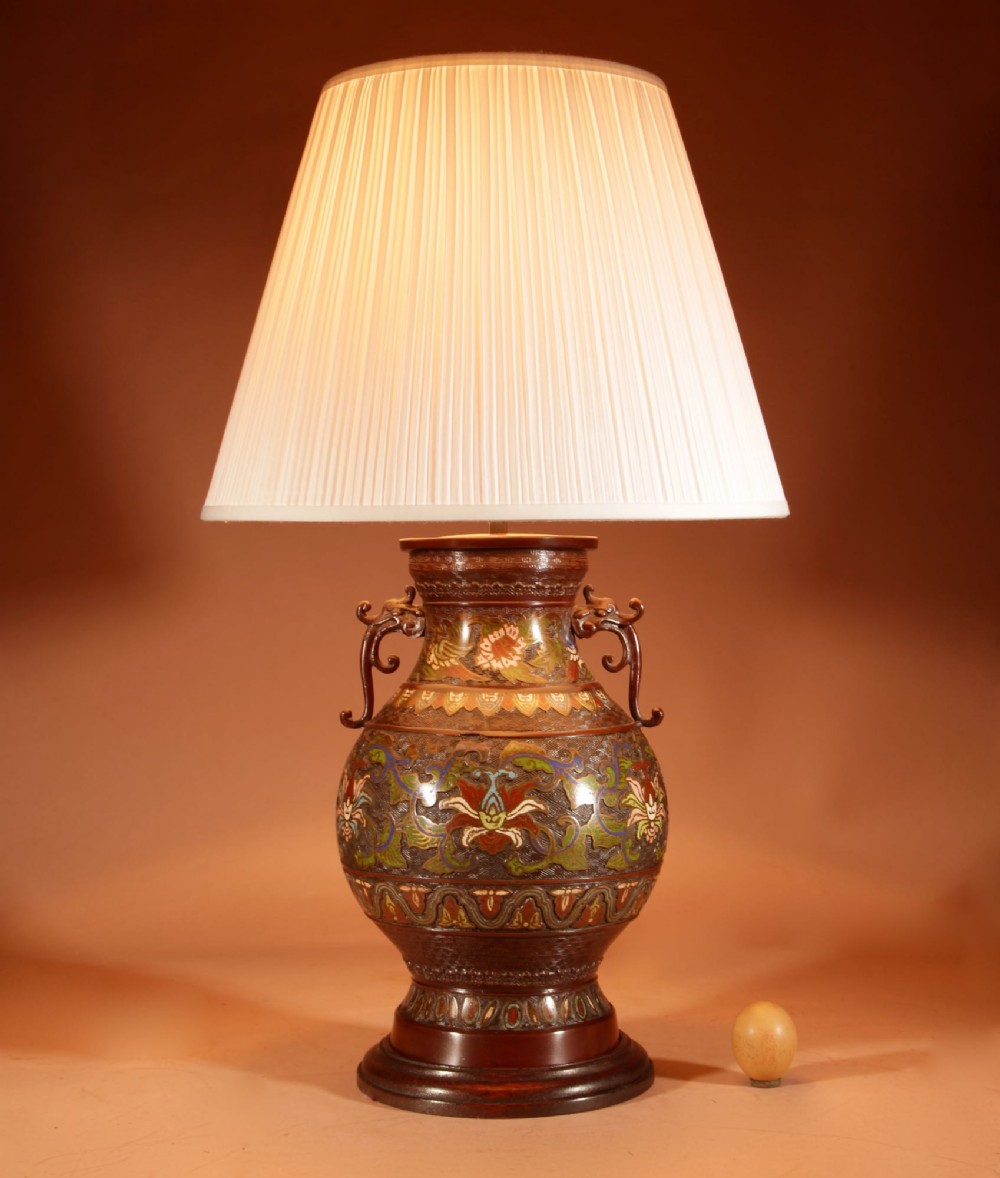 A Japanese champleve bronze vase lamp with ornate scroll handles and polychrome enamel detailing, topped with a pleated white shade.