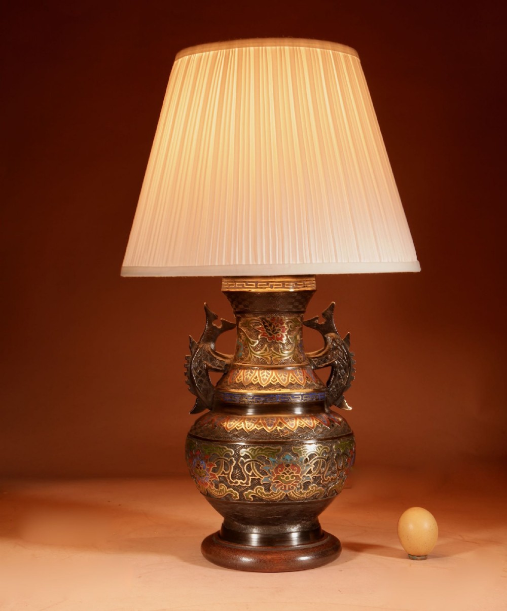 A Japanese champleve bronze vase-form table lamp featuring cast dragon handles, colourful geometric enamel inlay, and a cream pleated shade.