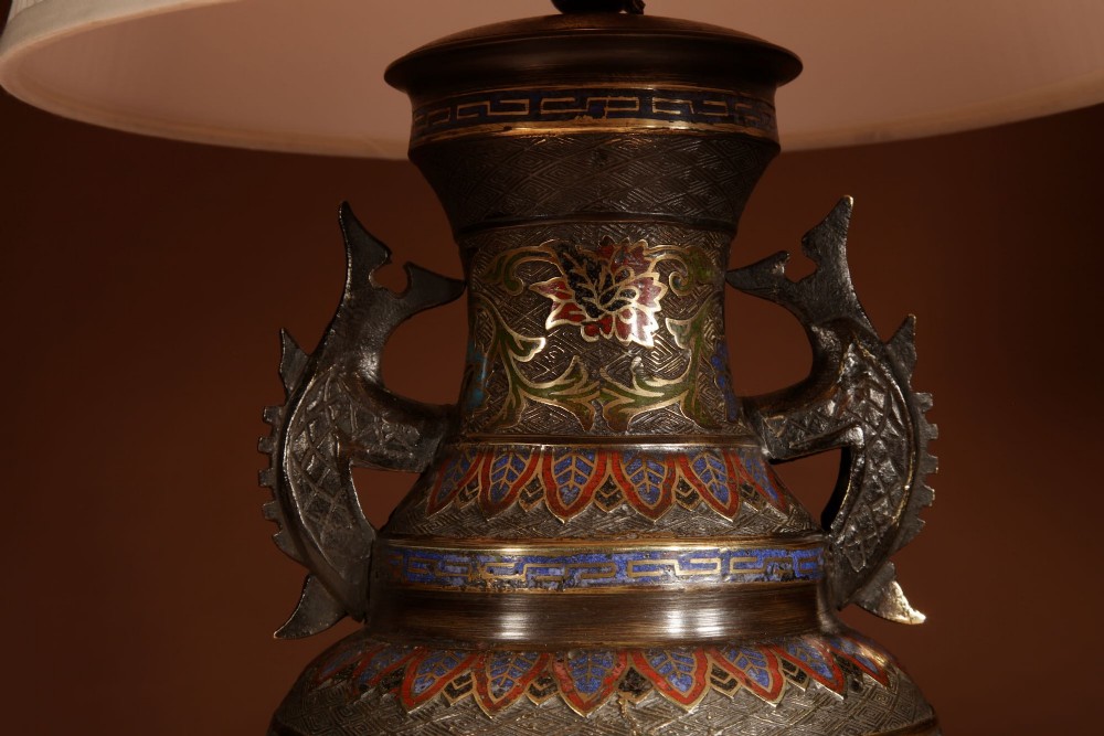 A Japanese champleve bronze vase-form table lamp featuring cast dragon handles, colourful geometric enamel inlay, and a cream pleated shade. View V