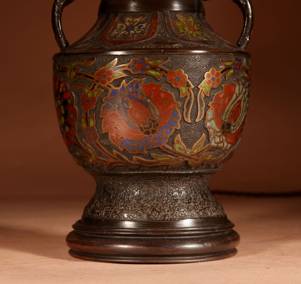 A Japanese champleve bronze urn formatted as a table lamp with polychrome enamel floral patterns, sculpted handles, and a cream pleated shade. View VII