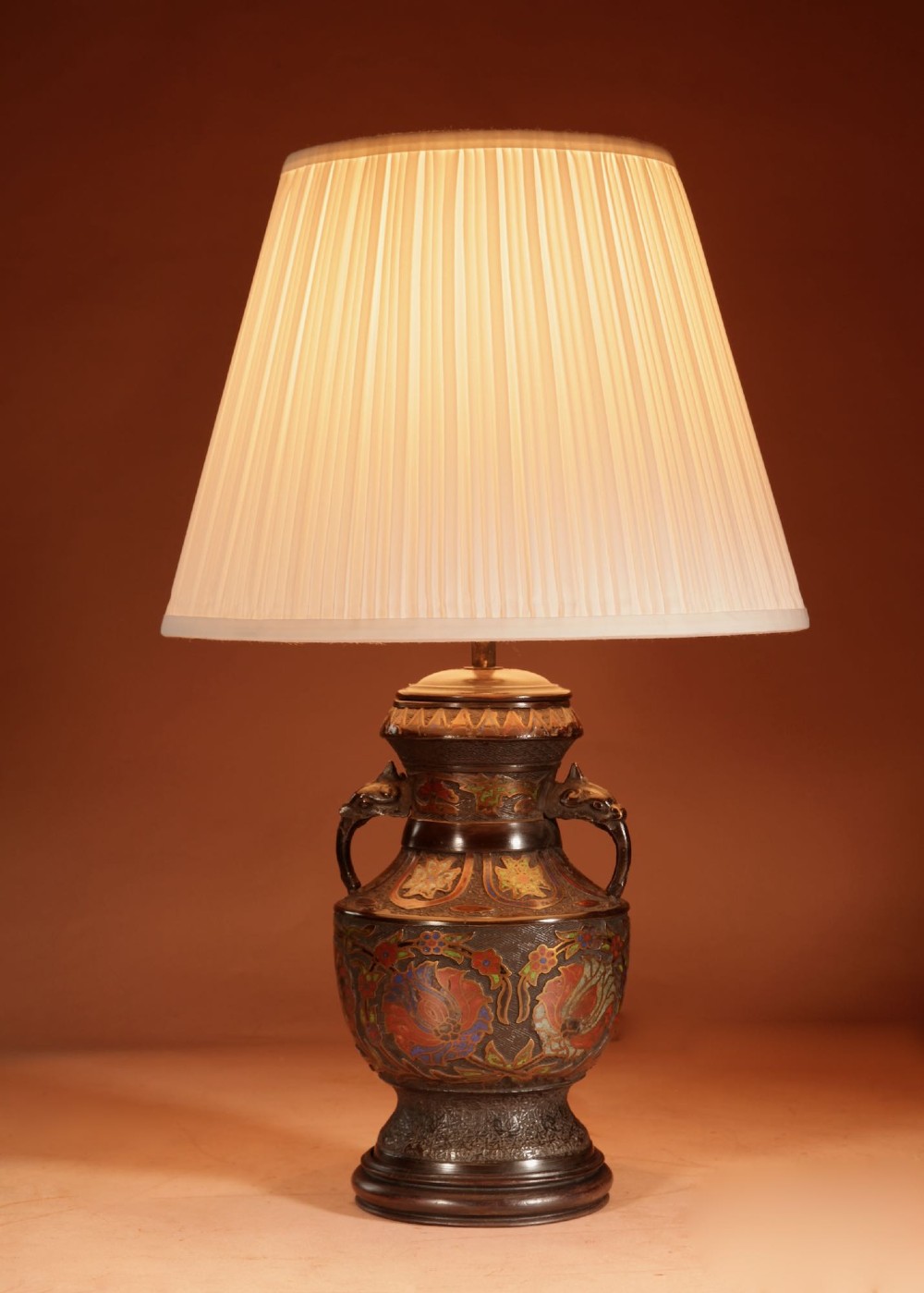 A Japanese champleve bronze urn formatted as a table lamp with polychrome enamel floral patterns, sculpted handles, and a cream pleated shade. View IX