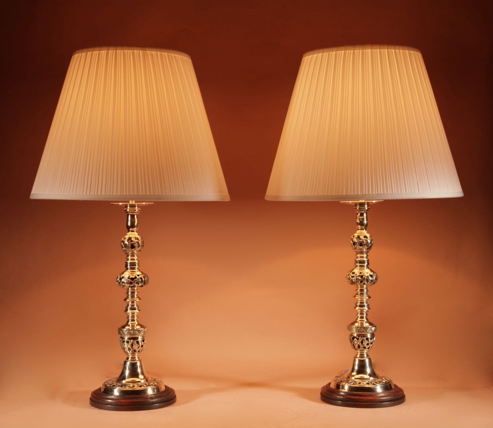 A pair of turned brass table lamps featuring openwork cast detailing and cream pleated shades set against a neutral background. View II