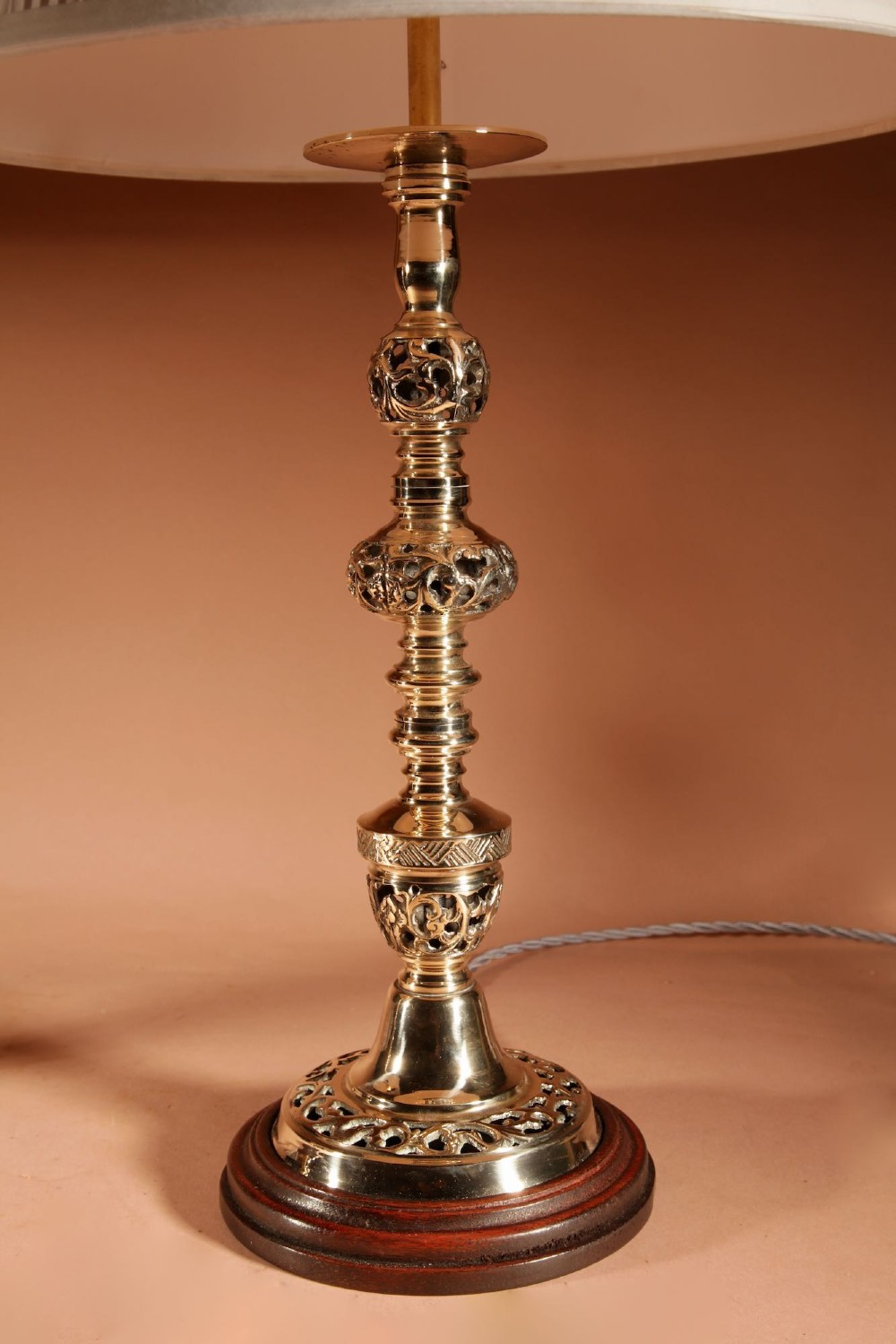 A pair of turned brass table lamps featuring openwork cast detailing and cream pleated shades set against a neutral background. View III