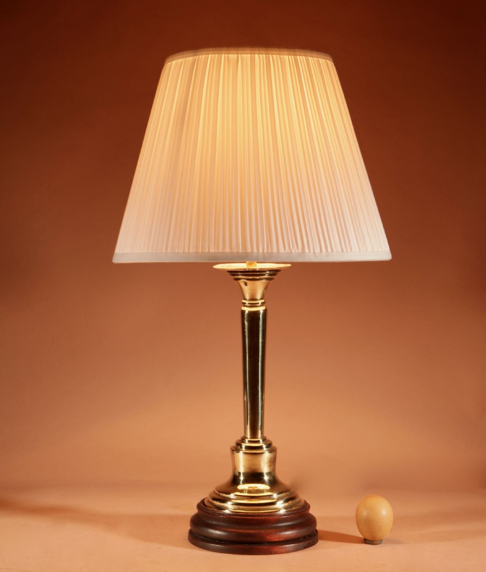 A polished brass column table lamp featuring a turned hardwood base and a cream pleated fabric lampshade.