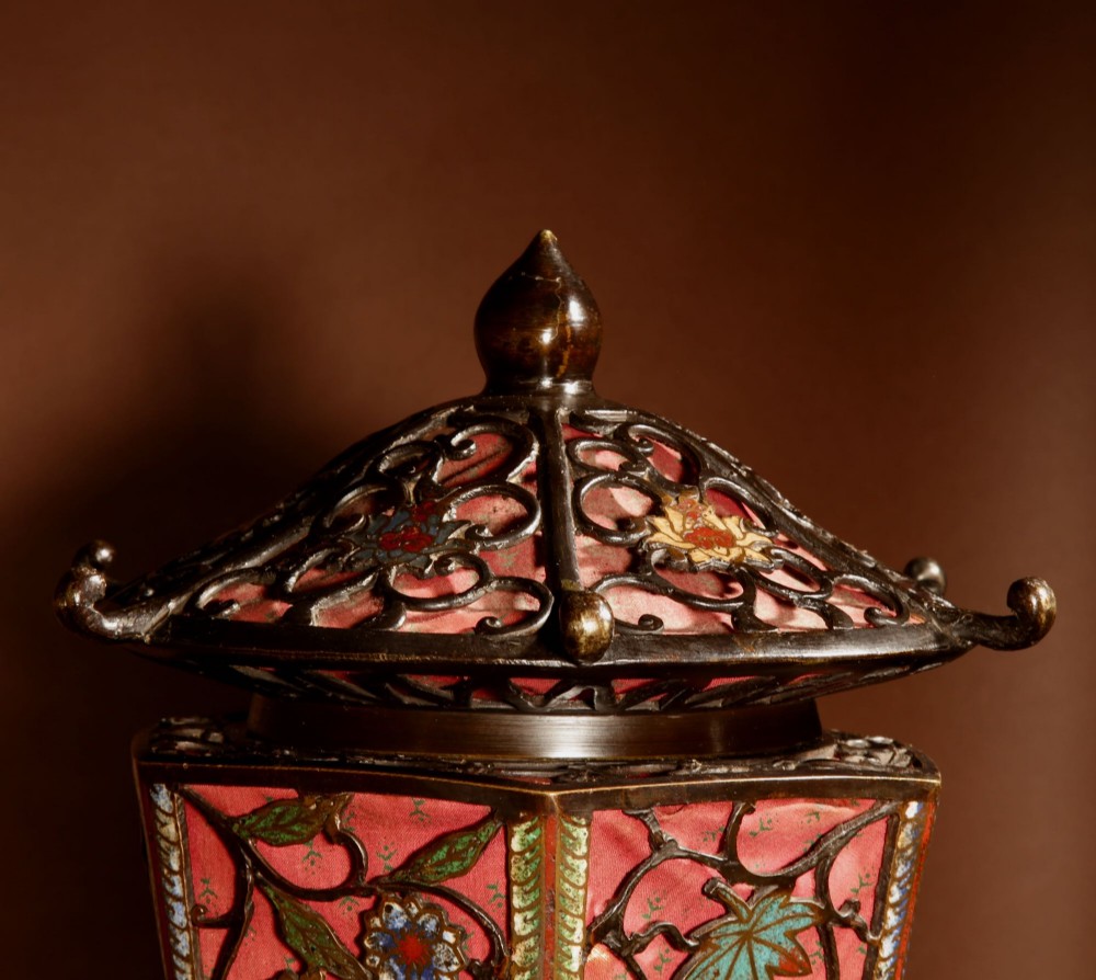 A tall Japanese bronze standard lamp featuring an illuminated red glass lantern shade with enamelled foliage motifs supported on a slender column base. View V