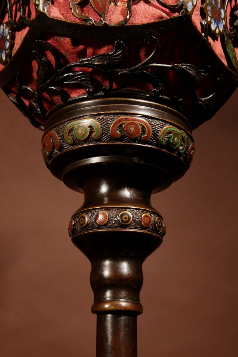 A tall Japanese bronze standard lamp featuring an illuminated red glass lantern shade with enamelled foliage motifs supported on a slender column base. View XI
