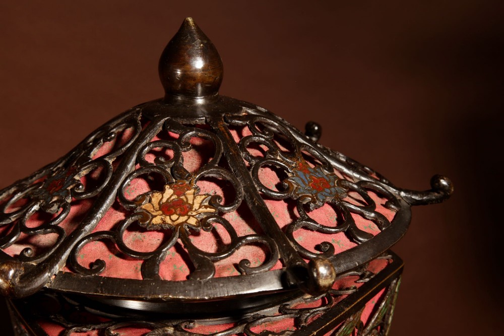 A tall Japanese bronze standard lamp featuring an illuminated red glass lantern shade with enamelled foliage motifs supported on a slender column base. View XII