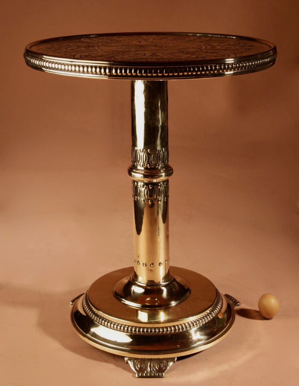 A circular polished brass side table featuring an embossed Art Nouveau floral pattern on top, supported by a central column pedestal and rounded base. View VI