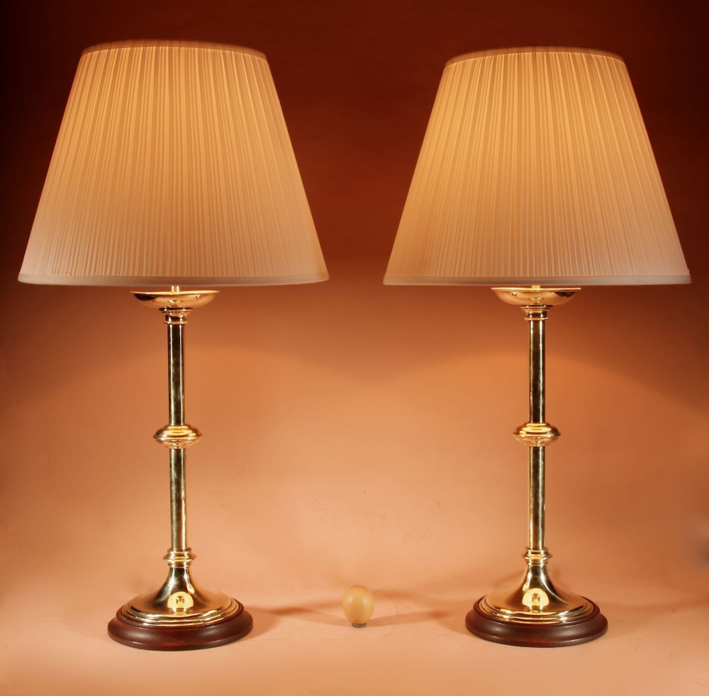 A pair of polished brass table lamps featuring knopped stems, circular timber bases, and cream pleated shades.