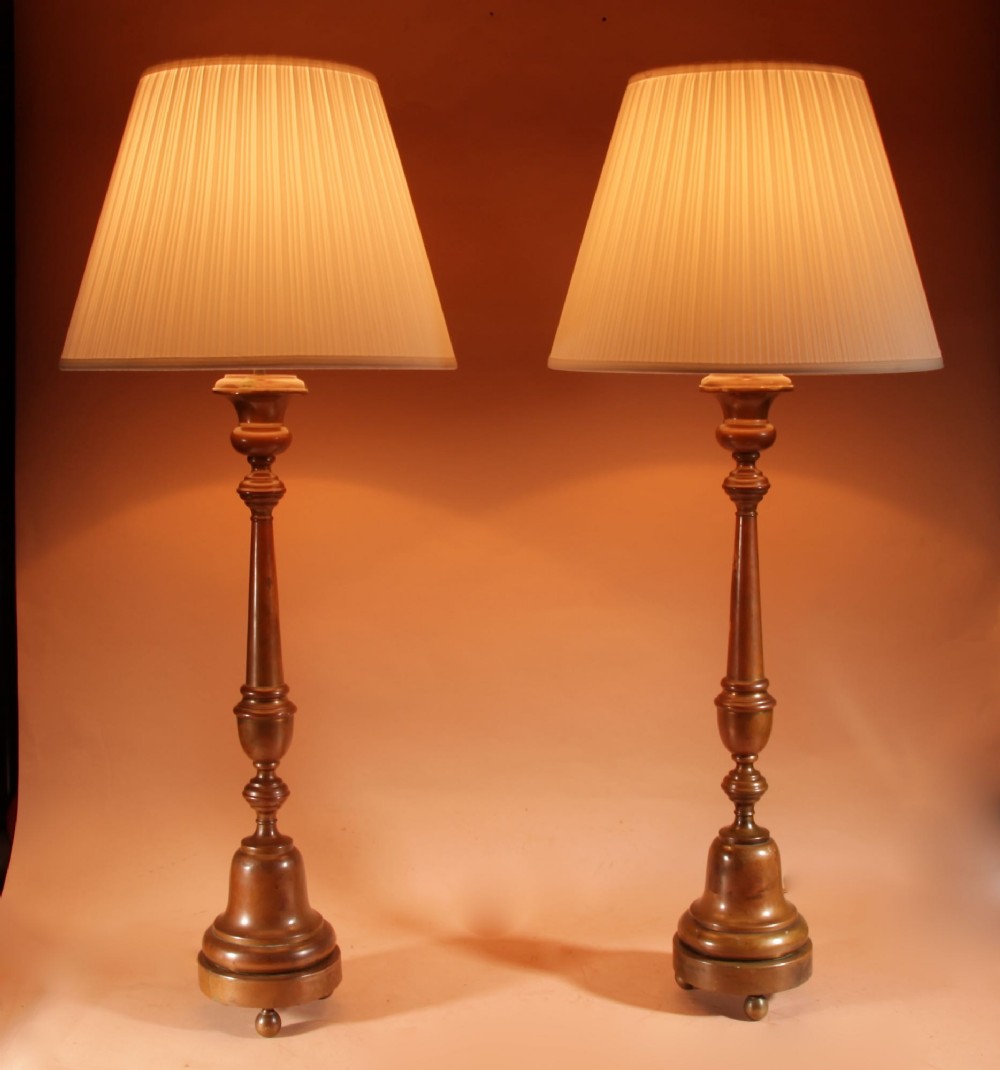 A pair of tall patinated brass candlestick table lamps featuring turned stems and pleated cream shades on circular bases. View II