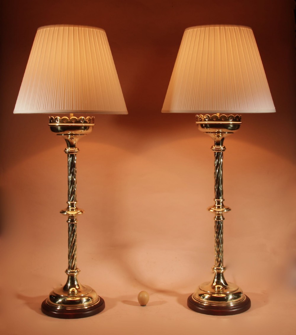 A pair of tall, polished brass Gothic style table lamps featuring spiral twist columns, wooden bases, and cream pleated shades.