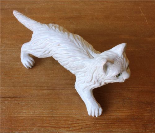 fig 2. A cream-glazed terracotta cat figure depicted in a crouching pose featuring bright green glass eyes.