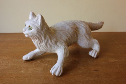 fig 3. A cream-glazed terracotta cat figure depicted in a crouching pose featuring bright green glass eyes.