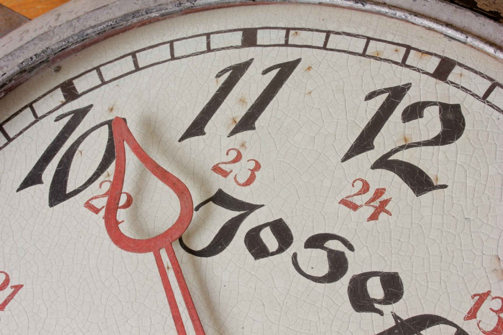 A large double-sided metal trade sign shaped like an oversized pocket watch, featuring black numerals, red clock hands, and an attached side mounting bracket. View IV