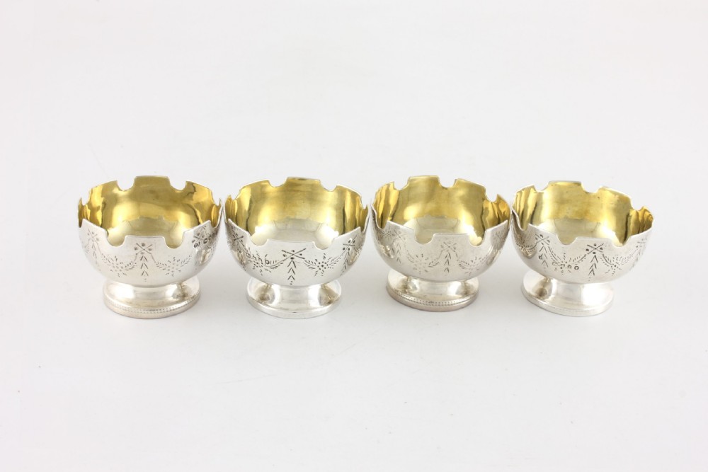 Set of four Victorian sterling silver salt cellars with scalloped rims, engraved foliate patterns, and gold-gilded interiors. View V