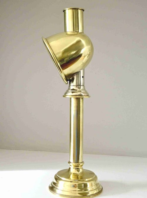 fig 1. Solid brass candle lamp featuring a circular stepped base, a vertical tubular stem, and a curved hooded cowl reflector enclosing an internal candle socket.