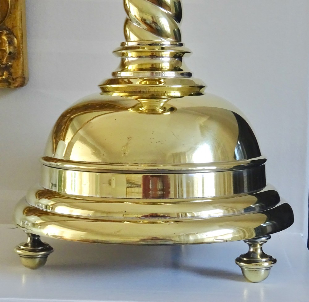A pair of polished brass candlesticks with barley twist stems, broad drip pans, and domed bases set on small ball feet. View V