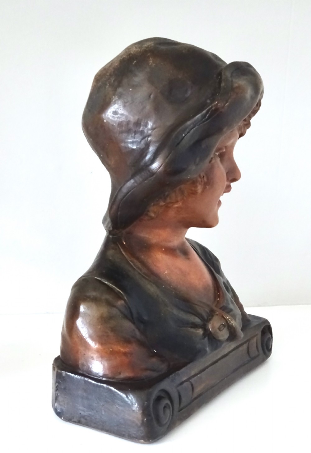A 1930s French polychrome plaster bust depicting a young child wearing a hat, set upon a dark rectangular plinth with scrolled corners. View II