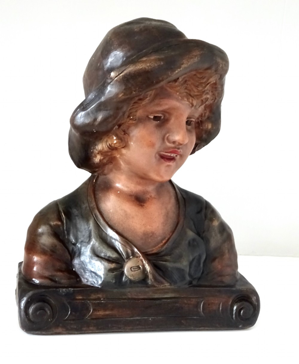A 1930s French polychrome plaster bust depicting a young child wearing a hat, set upon a dark rectangular plinth with scrolled corners.