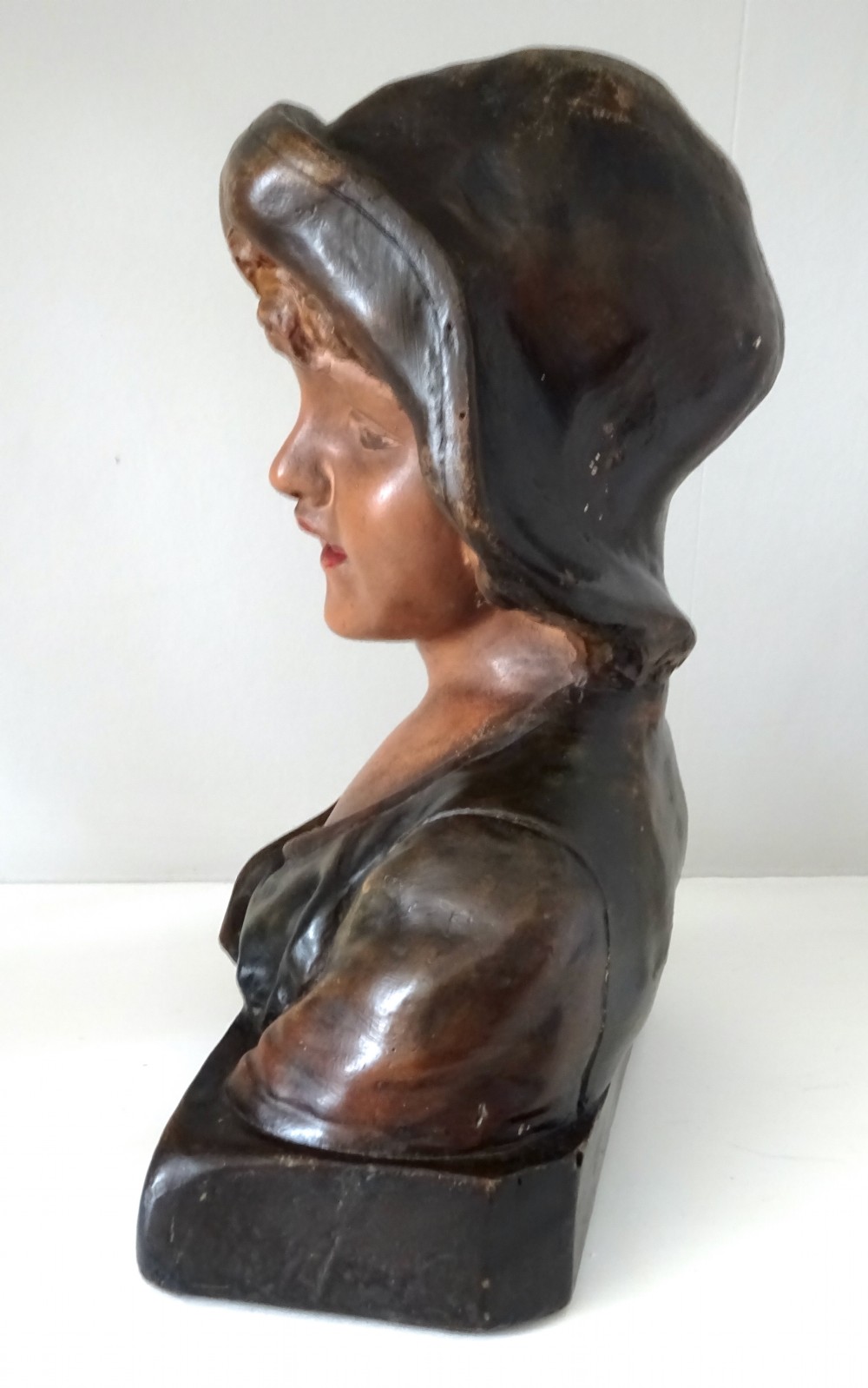 A 1930s French polychrome plaster bust depicting a young child wearing a hat, set upon a dark rectangular plinth with scrolled corners. View IV