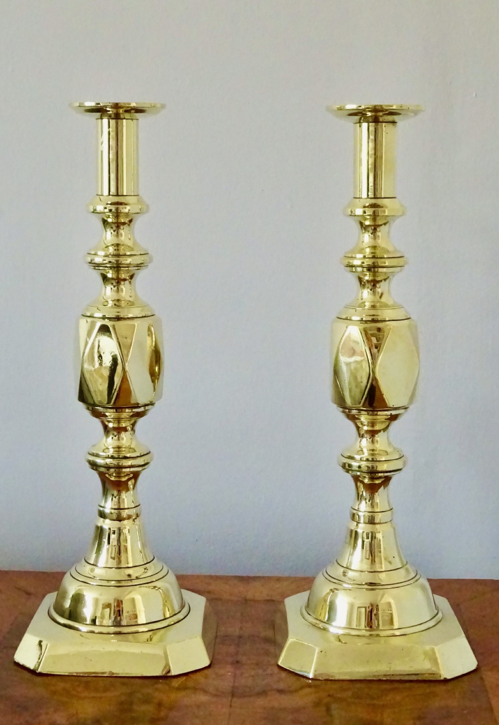 A pair of polished Victorian brass candlesticks with turned columns, faceted central knops, and square bases with cut corners. View V