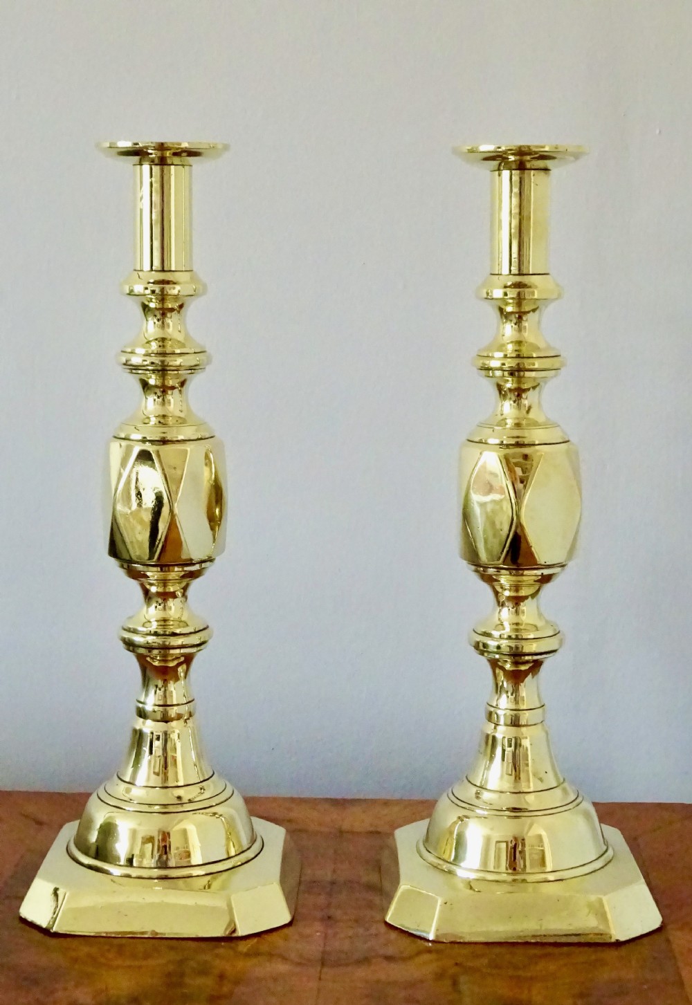 A pair of polished Victorian brass candlesticks with turned columns, faceted central knops, and square bases with cut corners.