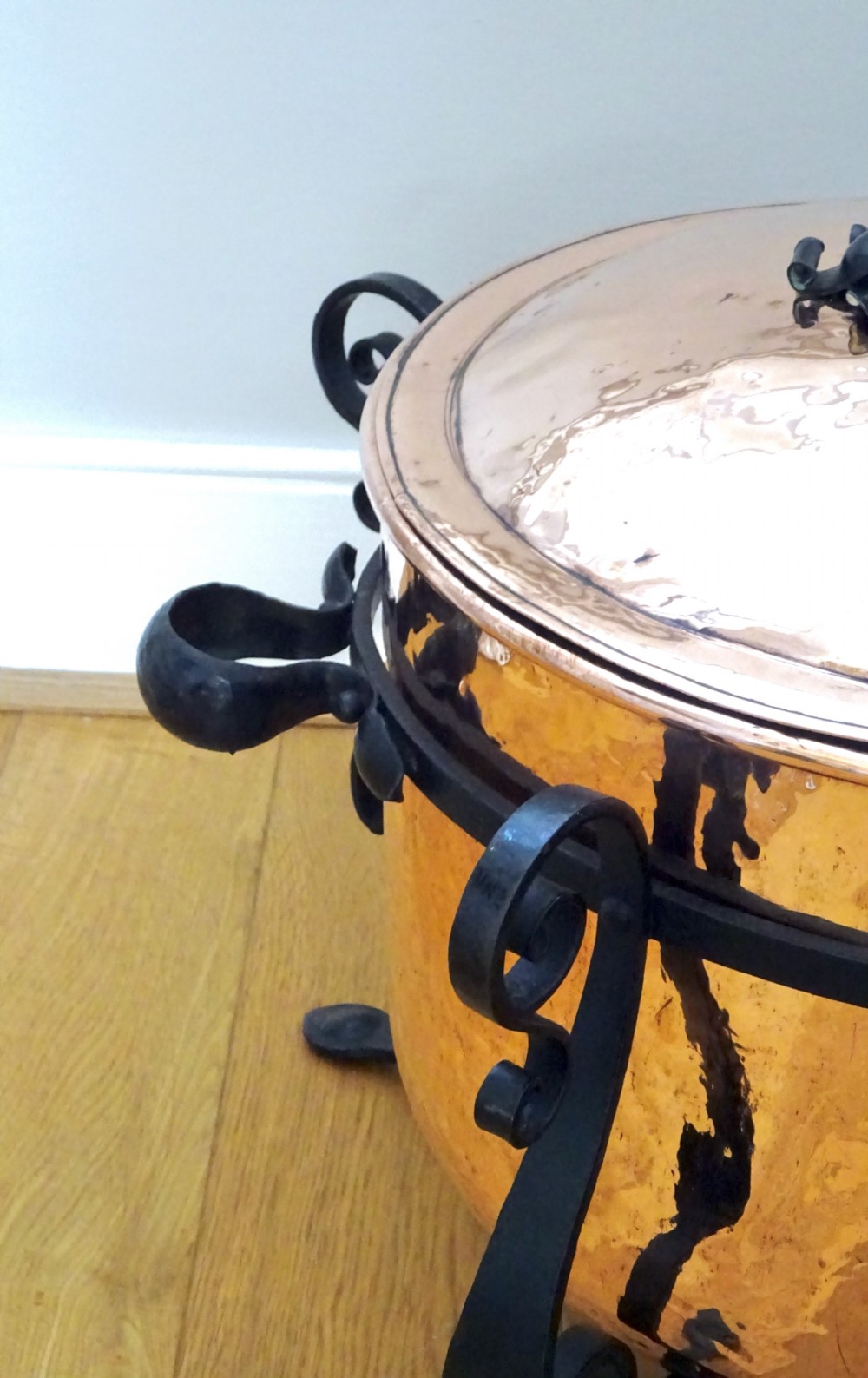 A large hammered copper bin with a domed lid fitted inside a black wrought iron stand with scrolled legs. View VI
